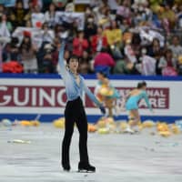 Hanyu salutes the crowd as \"flower girls\" collect stuffed Pooh bears and flowers that fans have thrown onto the ice. | DAN ORLOWITZ