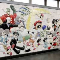 A woman looks at a large relief Monday depicting popular characters that appear in cartoons by the late cartoonist Osamu Tezuka. The relief was unveiled on the same day at Kokusai Tenjijo Station on the Rinkai Line in Tokyo to commemorate the 90th year since Tezuka was born. | KYODO