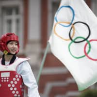 Miyu Yamada, a Japanese taekwondo competitor who won a bronze medal at the 2018 Asian Games in Jakarta, stands by one of two Olympic flags that were handed over to Tokyo from Rio de Janeiro, where the 2016 Olympic Games were held, during  an event outside Tokyo Station on Saturday. | RYUSEI TAKAHASHI