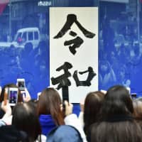 People snap photos with their smartphones of a placard displaying Japan\'s new era name, Reiwa, in front of the Wako department store in Tokyo\'s Ginza district on Monday. | KYODO