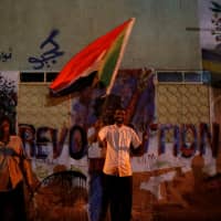 A Sudanese protester waves a national flag as he arrives a mass protest in front of the Defense Ministry in Khartoum on Sunday. | REUTERS