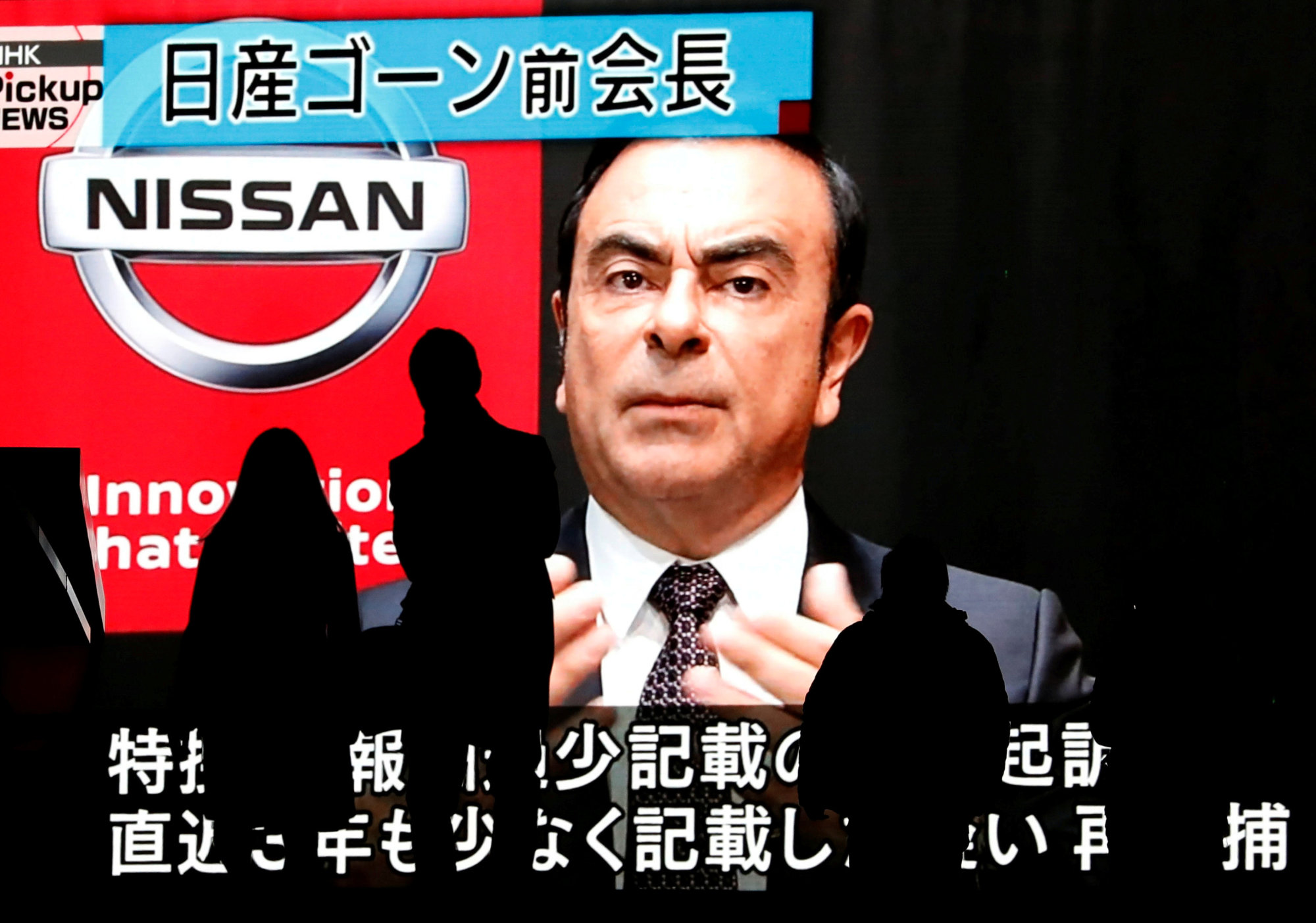 Passersby are silhouetted as a huge street monitor broadcasts news reporting ousted Nissan Motor chief's Carlos Ghosn's indictment and re-arrest in Tokyo in December. | REUTERS
