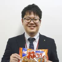 A Kameda Seika Co. employee holds a bag of crispy rice crackers with roasted peanuts, known as Kaki No Tane in Japan and Kameda Crisps abroad. | KYODO
