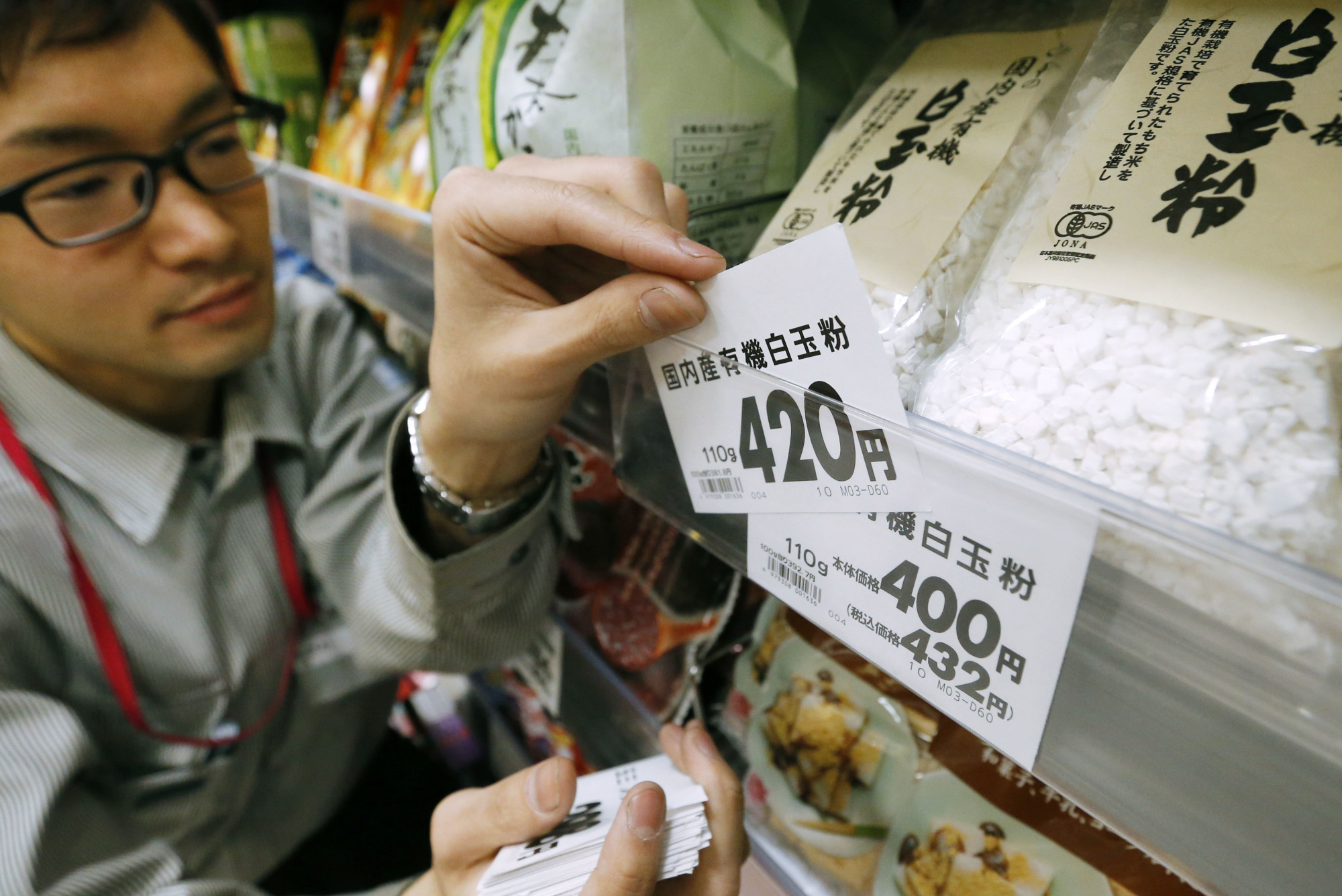A supermarket worker replaces a price tag before Japan raised the consumption tax to 8 percent from 5 percent in 2014. | KYODO