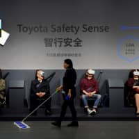 A cleaner walks past visitors wearing virtual reality (VR) goggles at a booth for Toyota Safety Sense during the media day for the Shanghai auto show in Shanghai Tuesday. | REUTERS