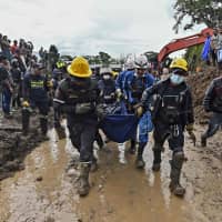 Rescue workers carry a corpse after a landslide in Rosas, Valle del Cauca department, in southwestern Colombia, on Sunday. At least 14 people were killed and five others injured by a mudslide that buried eight houses early Sunday. | AFP-JIJI