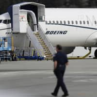 A worker walks next to a Boeing 737 MAX 8 parked at Boeing Field in Seattle March 14. U.S. aviation regulators said Monday Boeing needs more time to finish changes in a flight-control system suspected of playing a role in two deadly crashes. | AP
