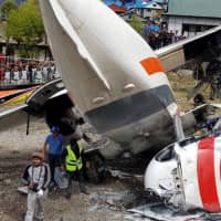 A parked helicopter lies on its side after an airplane crashed into it while taking off in Lukla, Nepal, Sunday. | ANG TASHI SHERPA / HANDOUT / VIA REUTERS