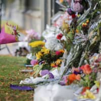 A little girl carries flowers to a memorial wall on March 17 following the mosque shootings in Christchurch, New Zealand, that left 50 dead and 39 wounded two days earlier. New Zealand\'s parliament on Wednesday passed sweeping gun laws that outlaw military-style weapons. | AP