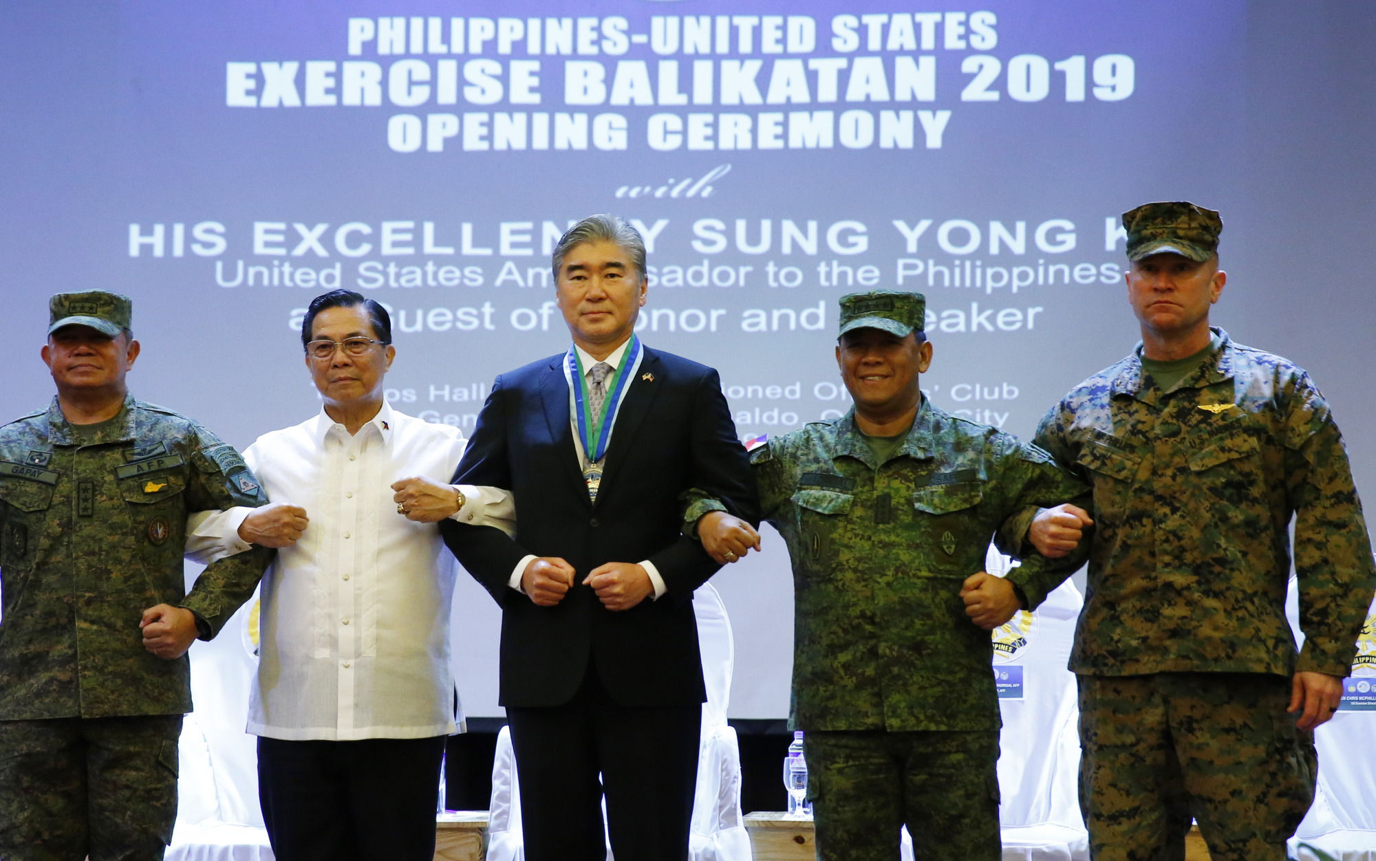 Philippine Armed Forces Southern Luzon Command Chief Lt. Gen. Gilbert Gapay (from left), Undersecretary of National Defense Cardozo Luna, U.S. Ambassador to the Philippines Sung Kim, Armed Forces of the Philippines Chief Gen. Benjamin Madrigal Jr. and Brig. Gen. Christopher McPhillips link arms during the opening ceremony of the joint U.S.-Philippine military exercise Balikatan 2019 on Monday at Camp Aguinaldo, northeast of Manila. | AP