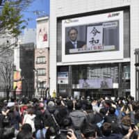 People near Tokyo\'s Shinjuku Station watch the announcement of the new era on a large monitor.  | KYODO