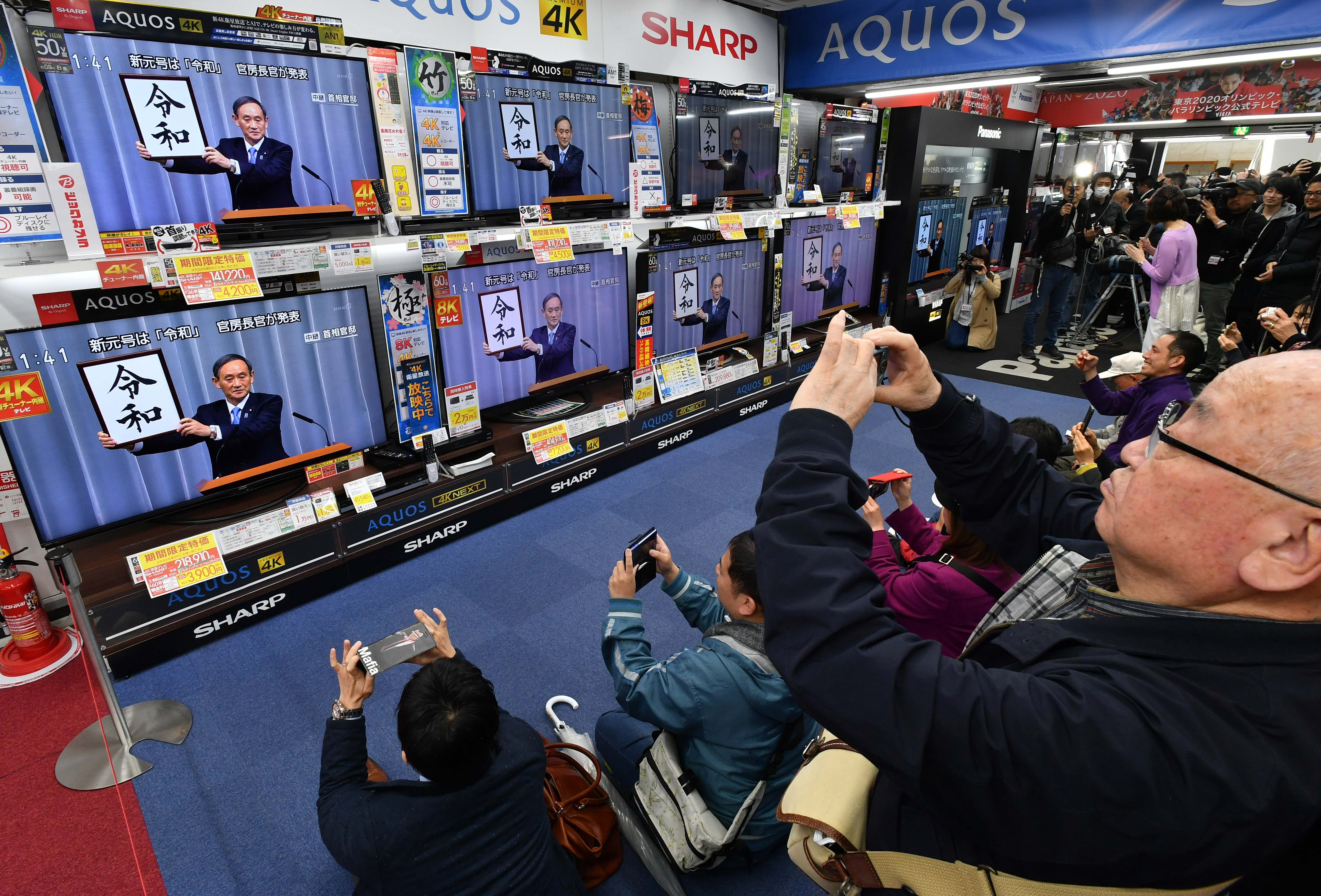People watch TVs at an electronics store in Tokyo's Yurakucho district Monday as the new Imperial era name, Reiwa, is unveiled by Chief Cabinet Secretary Yoshihide Suga at a televised news conference.  | YOSHIAKI MIURA 