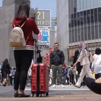 A woman takes a photo at Tokyo\'s famed Shibuya scramble crossing earlier this month. Many travelers end up sightseeing while dragging along their suitcases because it is often difficult to find an empty coin locker large enough to accommodate big pieces of luggage. | MAGDALENA OSUMI