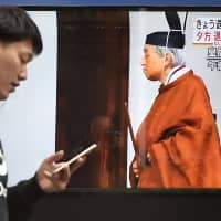 A man walks along a street past a monitor showing TV reports on the abdication of Emperor Akihito in Tokyo on April 30. | AFP-JIJI