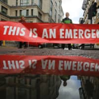 Climate activists from the Extinction Rebellion group block the road as they demonstrate outside the offices of Deutsche Bank in London on April 25. | BLOOMBERG