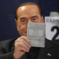 Former Italian Prime Minister Silvio Berlusconi holds up his ballot for the European Parliament elections at a polling station in Milan, Italy, Sunday. | AP