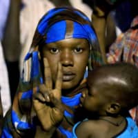 A Sudanese woman holding a baby flashes the \"V\" for victory sign as protesters gather outside the military headquarters in Khartoum demanding the instalment of civilian rule on Monday. Thousands of Sudanese men and women have held an around-the-clock sit-in at the site since April 6, initially to seek the military\'s support in toppling longtime autocrat Omar Bashir and later to remove the generals who seized power after his ouster. | AFP-JIJI