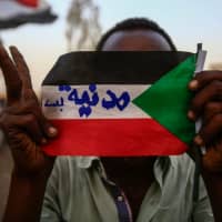 A Sudanese protester holds the national flag with writings reading in Arabic \"Civilian Only\" during a rally outside the army headquarters in Khartoum May 2. The U.S. pressed Sudan\'s military leader Wednesday to reach an agreement with protesters, who have threatened a disobedience campaign unless there is a transfer to civilian rule. | AFP-JIJI