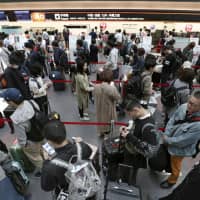 People form a long line Wednesday at a Japan Airlines check-in counter, at Haneda airport in Tokyo, after the airline\'s automated check-in system suffered a system glitch. | KYODO