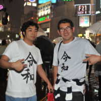 Two men wearing T-shirts printed with the Reiwa kanji character pose for a photo before the dawn of the Reiwa Era at the scramble crossing in front of Tokyo\'s Shibuya Station on Tuesday. | KAZUAKI NAGATA