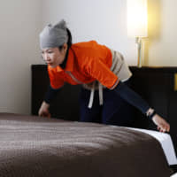 A Vietnamese woman working for a cleaning company in the city of Kochi spreads a sheet on a bed at a business hotel in January. The government is considering adding the hotel industry to its technical intern program for foreign nationals. | KYODO
