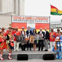 On May 3, the Festival de Camino a Latinoamerica was held in Odaiba. Above: Angela Karin Ayllon Quisbert, Bolivian charge d\'affaires ad interim (back row, center), poses with (from back row, left) Hidejiro Mimura of the association of cultural exchange between Latin America and Japan; Ryuusuke Ohki, secretary-general of the Tokyo Waterfront City Association; Hidehiro Tsubaki, chairman of the Japan-Bolivia Association; Shinji Minami, director of the Foreign Ministry\'s Latin American and Caribbean Affairs Bureau, South America Division; and the Bolivia Dance Company during a Sicuriada parade celebrating the 120th anniversary of Japanese immigration to Bolivia. | YOSHIAKI MIURA