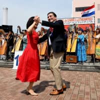 Paraguayan Ambassador Raul Florentin Antola (right) dances to music played by 104 arpa (Paraguayan harp) musicians to celebrate the 100th anniversary of diplomatic relations between Japan and Paraguay. | YOSHIAKI MIURA