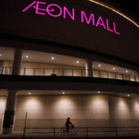 A woman rides past an Aeon shopping mall in Chiba in January 2018. | BLOOMBERG