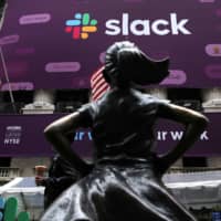 The Slack Technologies Inc. logo is seen behind the \"Fearless Girl\" statue outside the New York Stock Exchange (NYSE) during the company\'s direct listing in New York Thursday. | REUTERS