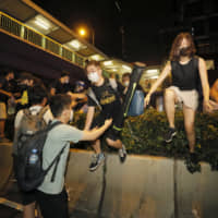 Protesters climb over a barrier near the Legislative Council in Hong Kong during the early hours of Monday. | AP