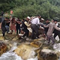 Local residents help accident survivors cross a river after a bus carrying some 50 passengers fell into a 150-meter (500-foot) gorge near Banjar, in the mountainous Kullu district of the Indian state of Himachal Pradesh, on Thursday. | AFP-JIJI