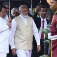 Indian Prime Minister Narendra Modi and Sri Lankan President Maithripala Sirisena walk under an umbrella as they attend a welcoming ceremony for Modi at the Presidential Secretariat in Colombo on Sunday. | AFP-JIJI