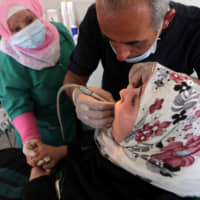 Bassel Maarawi, 57, a dentist, treats a displaced Syrian refugee at a mobile dental clinic in a truck near Azaz, Syria, June 16. | REUTERS