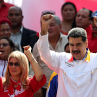 Venezuelan President Nicolas Maduro and his wife, Cilia Flores, greet people during a rally in support of the government in Caracas in May. | REUTERS