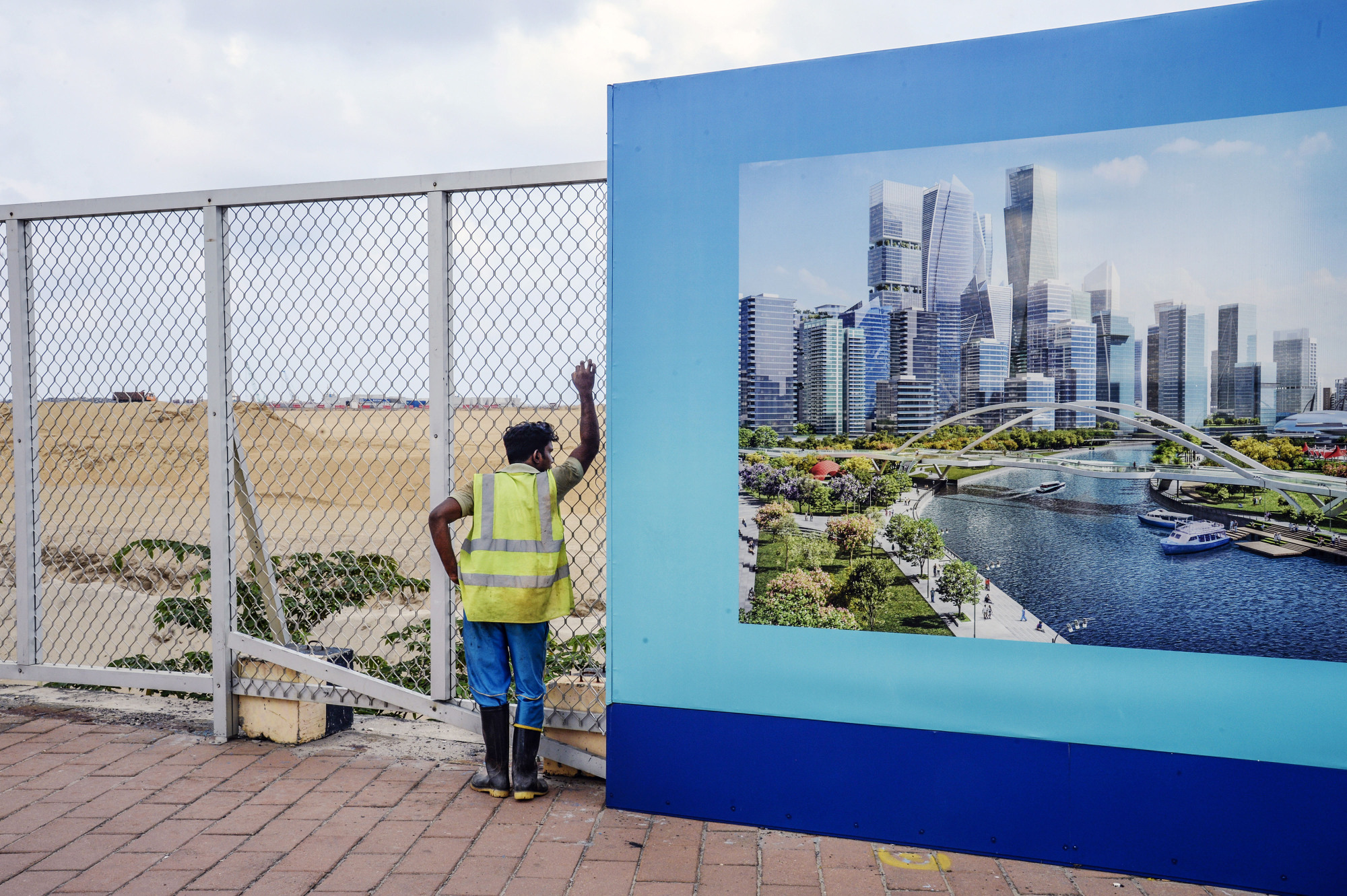 A worker at the site of Colombo Port City stands by a billboard featuring an artist's impression of the Colombo International Financial City project, both developed by China Harbour Engineering Co., in Colombo in March 2018. | BLOOMBERG