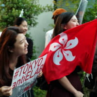 A protester holds the Hong Kong flag on Thursday in Tokyo during a rally against a controversial extradition bill. About 300 people joined the demonstration in front of the Hong Kong Economic and Trade Office. | RYUSEI TAKAHASHI