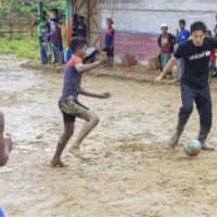 Makoto Hasebe plays soccer with Rohingya children on a muddy field at the Kutupalong refugee camp on Thursday. | KYODO