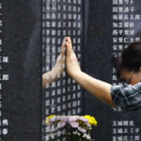 A woman touches the engraved name of a relative who perished in the Battle of Okinawa on the Cornerstone of Peace monument in Peace Memorial Park in Itoman, Okinawa Prefecture, on Sunday, which marked the 74th anniversary of the end of the bloody 1945 battle. | KYODO