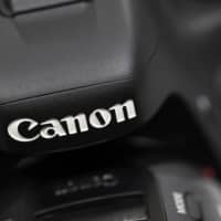 Canon Inc.\'s logo is seen on its mirrorless camera. The company\'s group net profit for this business year is now projected to fall by 36.7 percent from a year earlier due to the weakening demand for cameras in the Chinese market. | BLOOMBERG