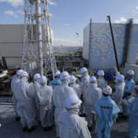 Media members in protective suits and masks receive a briefing from employees of Tokyo Electric Power Company Holdings Inc. at the Fukushima No. 1 nuclear power plant in Fukushima Prefecture in February 2016. | VIA BLOOMBERG