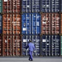 A worker walks in front of shipping containers stacked at a terminal in Tokyo in March. | BLOOMBERG