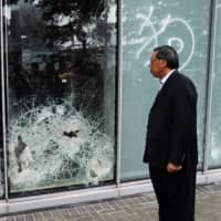 Andrew Leung, president of Hong Kong\'s Legislative Council, looks at damaged glass panels on Tuesday, a day after protesters broke into the council building. | REUTERS