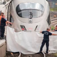 Policemen and fireworkers hold a white blanket as a visual cover at the site of a deadly attack at the railway station in Frankfurt am Main on Monday. An 8-year-old boy died and his mother was injured when a man pushed them in front of a train, police said. | ANDREAS ARNOLD / DPA / VIA AFP-JIJI