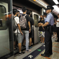 A police officer stands next to some protesters who are blocking the door of a train at a subway platform in Hong Kong on Tuesday. Protesters in Hong Kong have disrupted subway services during the morning commute by blocking the doors on trains, preventing them from leaving the stations. | AP