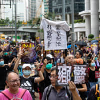 Demonstrators hold up signs while marching towards Causeway Bay during a protest in the Central district of Hong Kong on Sunday. | BLOOMBERG