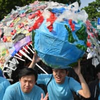 Indonesians protest against single-use plastics in Jakarta on July 21. Behind them is an anglerfish made out of plastic waste. | AFP-JIJI