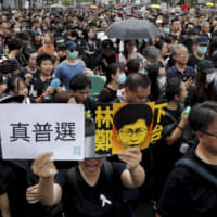 Protesters holding a caricature of Hong Kong Chief Executive Carrie Lam bearing the words \"Step down\" and \"Real election,\" take part in a march in Hong Kong on Sunday. | AP