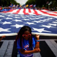 A girl helps carry a U.S. flag as she takes part in a parade during Fourth of July celebrations in Washington. | REUTERS