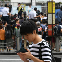 A man looks at his smartphone as a candidate for Sunday’s Upper House election stumps on July 15 in Tokyo’s Shibuya Ward. | YOSHIAKI MIURA