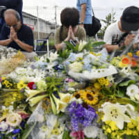 People pray in front of bouquets left for victims of the arson attack at a Kyoto Animation studio in Kyoto on Friday. | KYODO